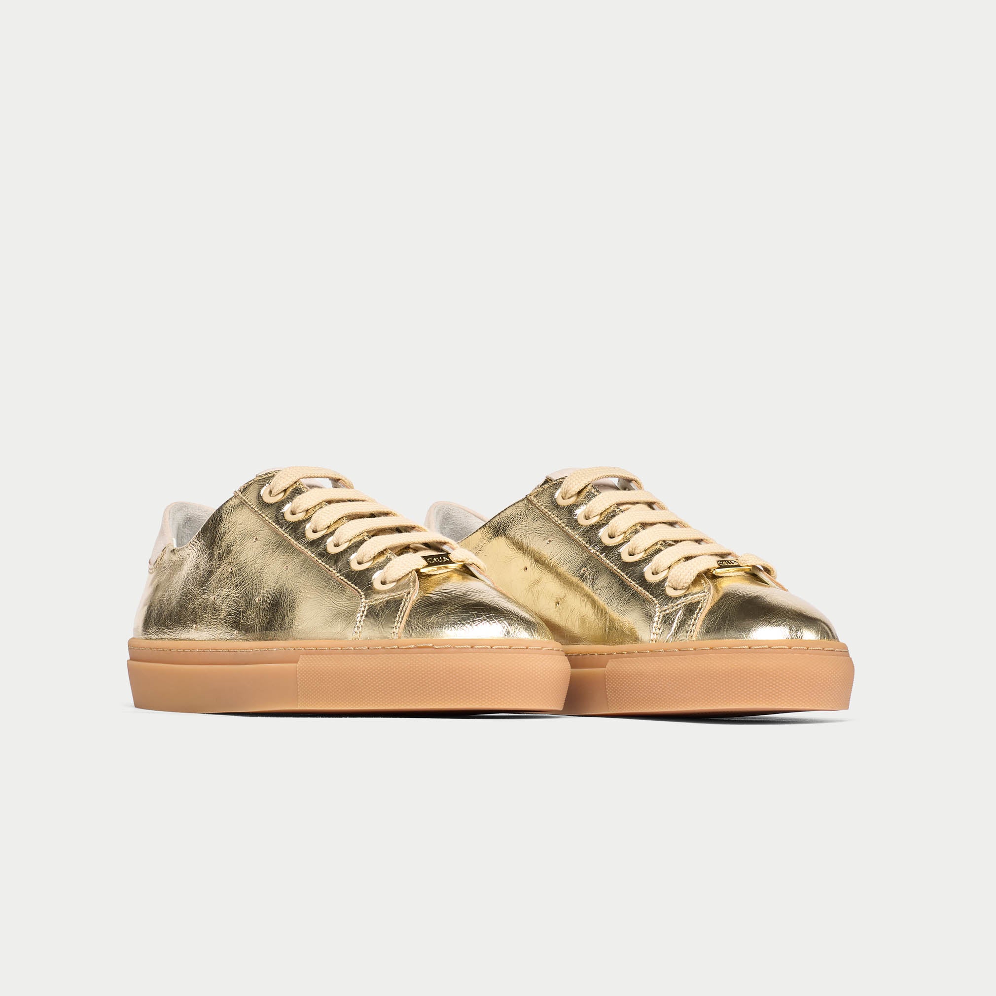 Pair of gold sneakers with brown soles on a light gray background