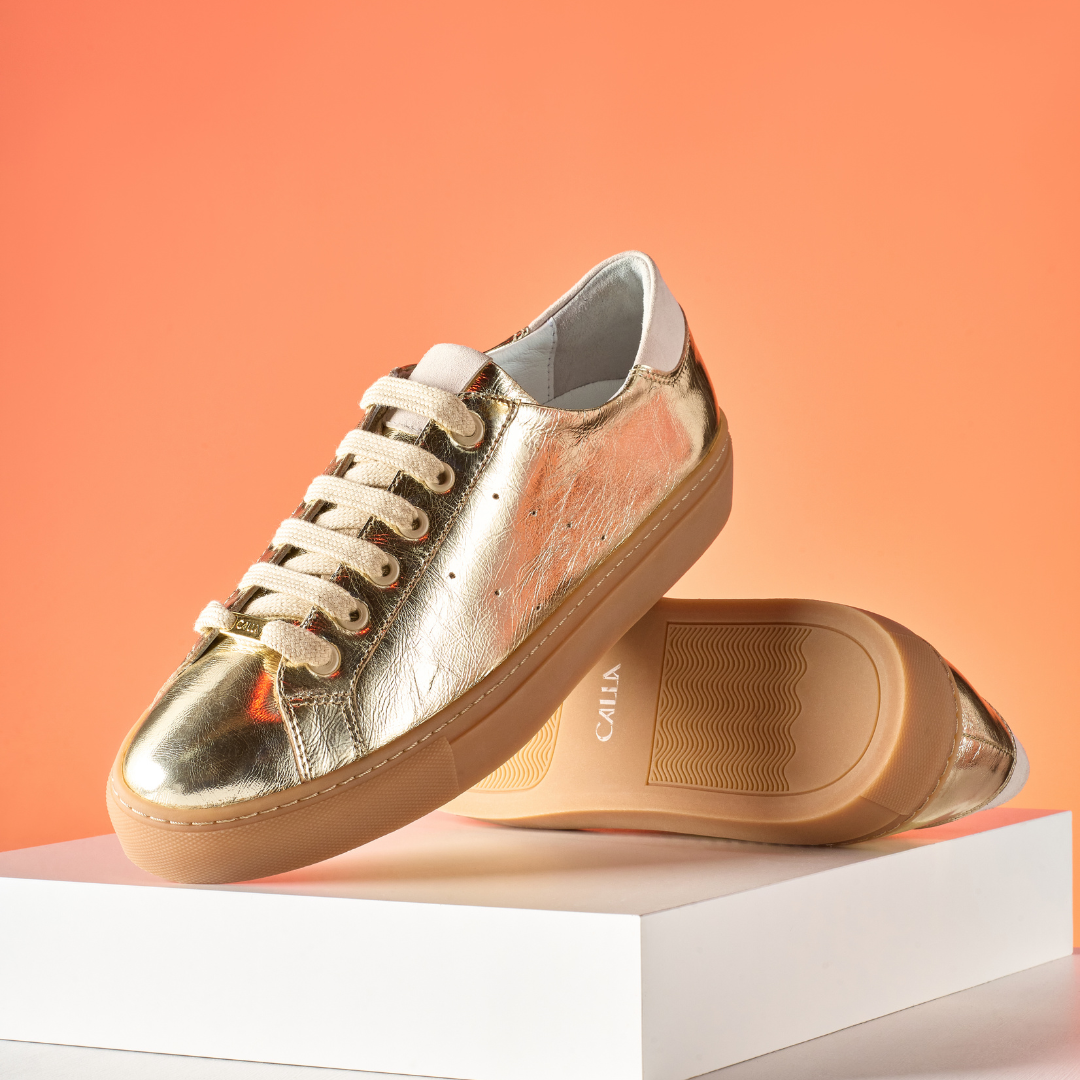 Gold sneaker with beige laces on an orange background
