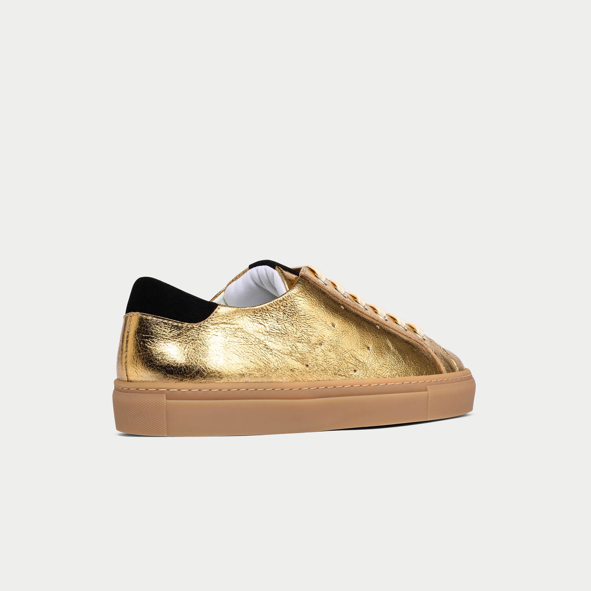 Gold sneaker with black heel on a white background