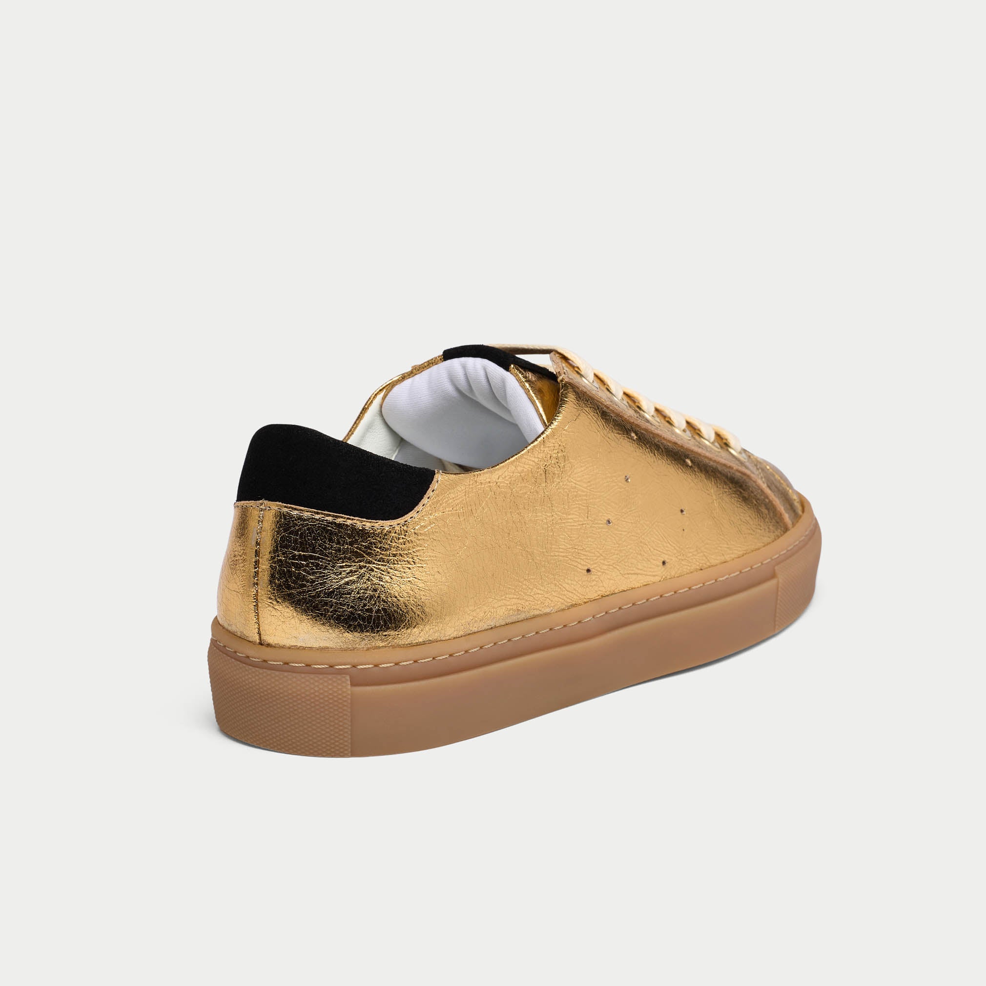 Gold sneaker with black sole on a light gray background