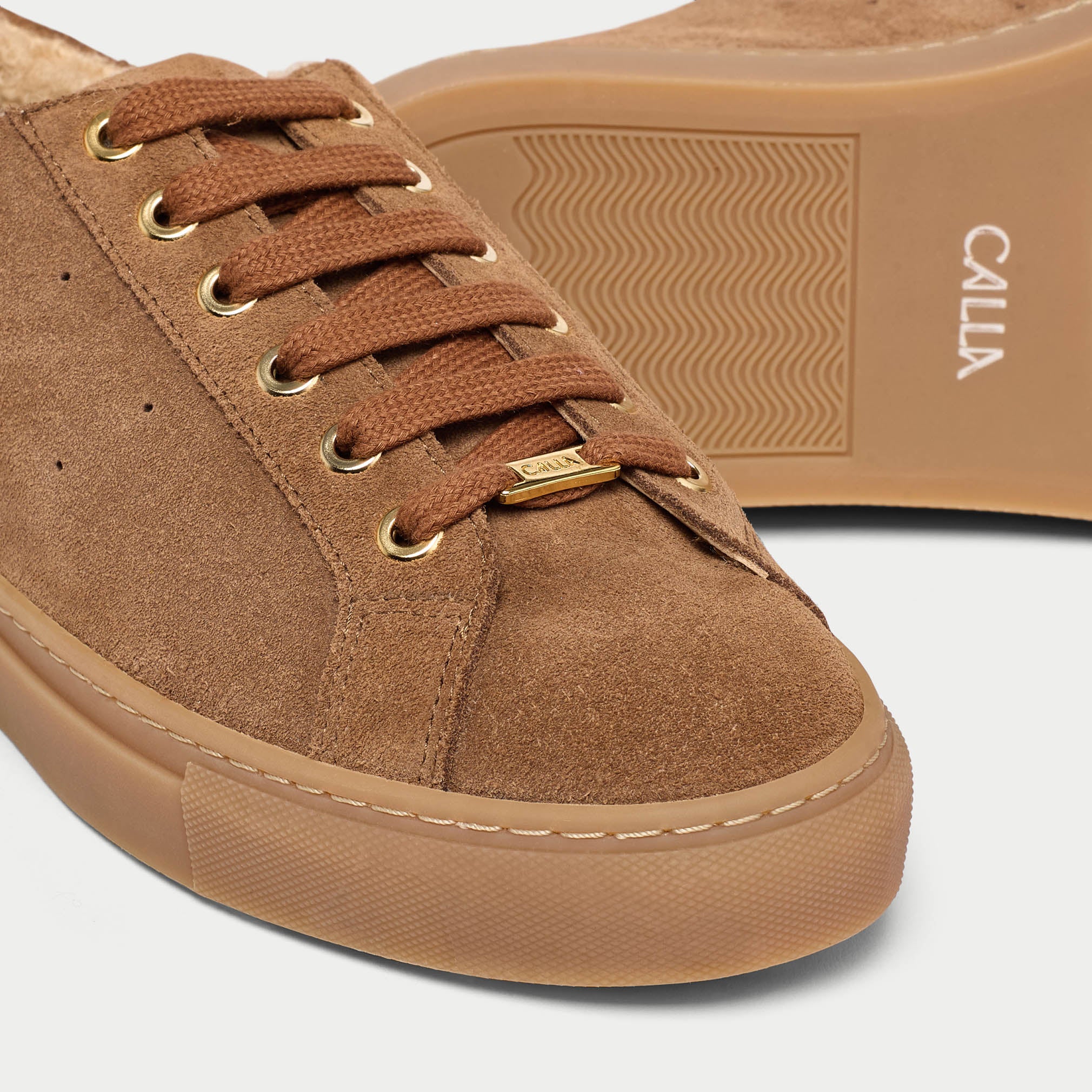Brown suede sneaker with gold laces on a light gray background