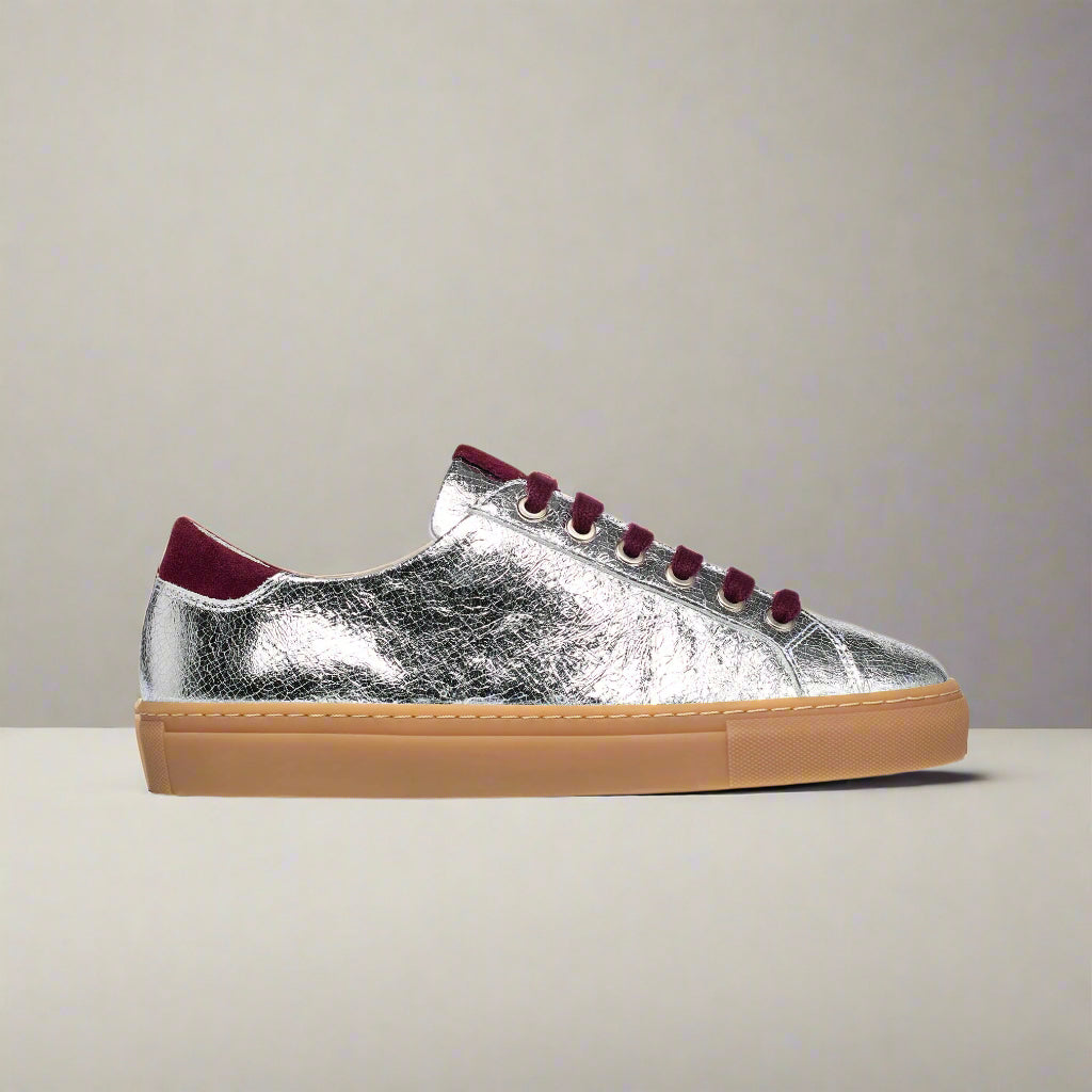 Silver sneaker with burgundy laces and sole on a light gray background