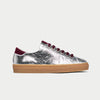 Silver sneaker with burgundy laces and sole on a light gray background