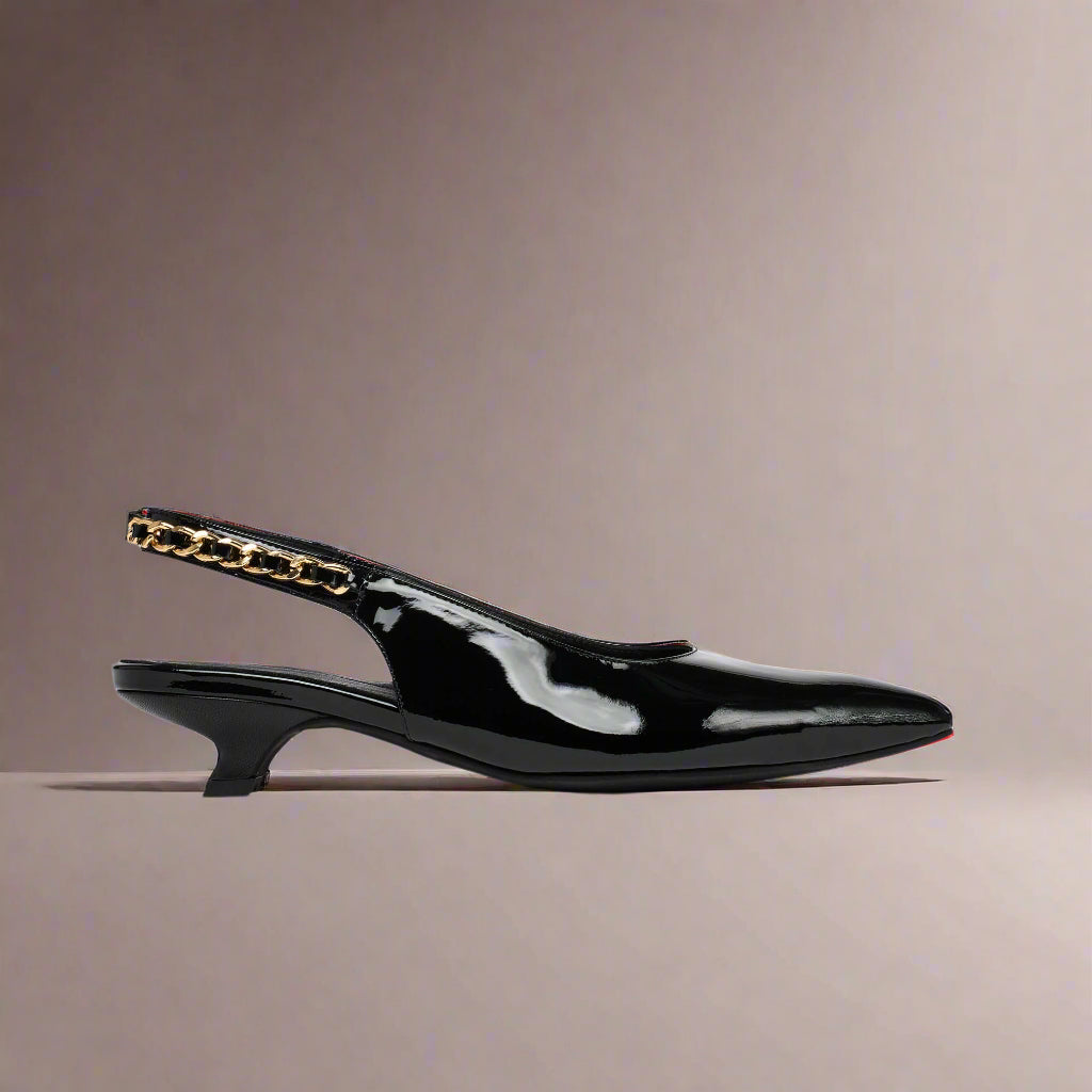 Black Thea patent leather slingback shoe with gold chain detail on a beige background