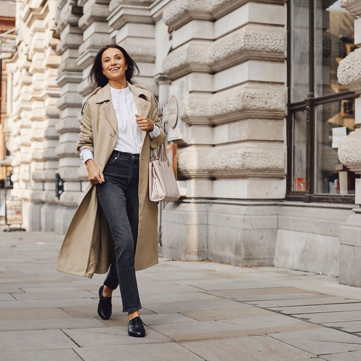 woman walking down street in jeans, camel coat, and black shoes